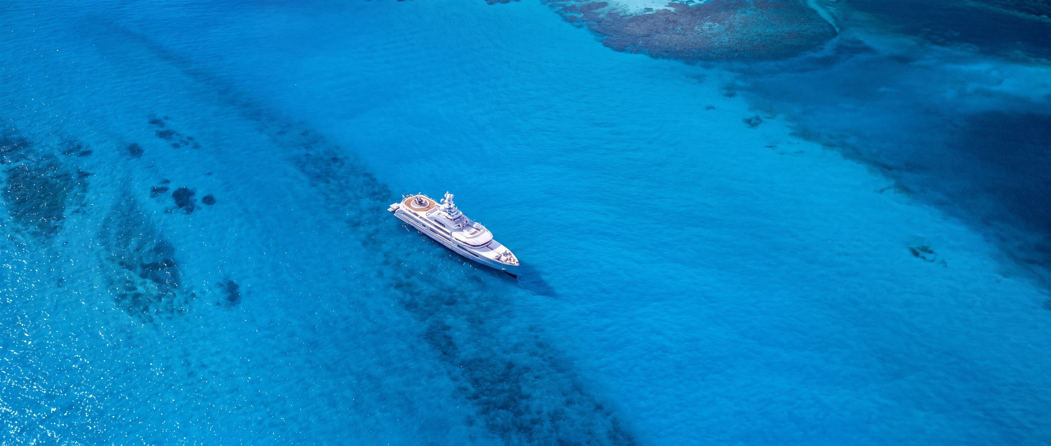 Aerial photograph of a superyacht at anchor over turquoise water